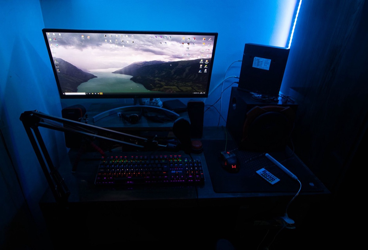 gamer in dark room with RGB keyboard and curved monitor